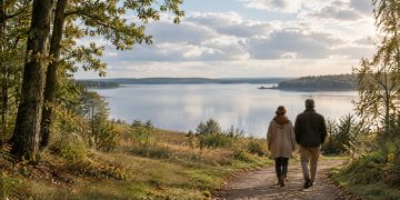 A couple walking along a wooded path towards a calm lake beneath soft September clouds in Denmark.